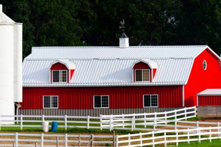 Red barn with white fencing, silos, and lush green background at Steel Commander Corp.