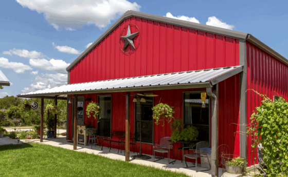 Red Barndominium on a blue sky sunny day with a porch and hanging plants