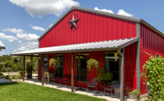 Red Barndominium on a blue sky sunny day with a porch and hanging plants