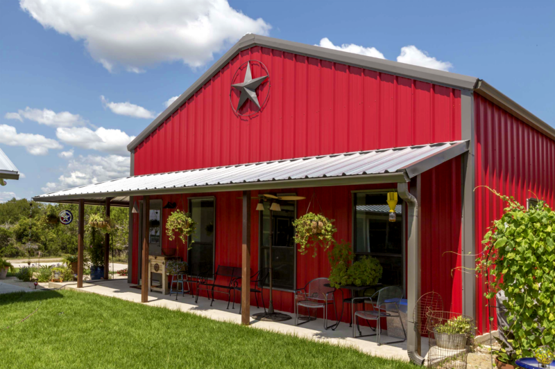 Red Barndominium on a blue sky sunny day with a porch and hanging plants